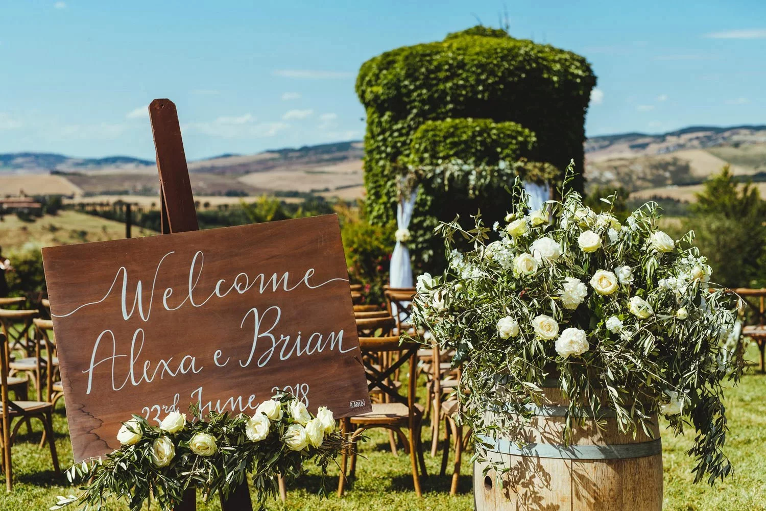 A sign reads 'Welcome Alexa e Brian' at a beautiful outdoor wedding ceremony in Tuscan.