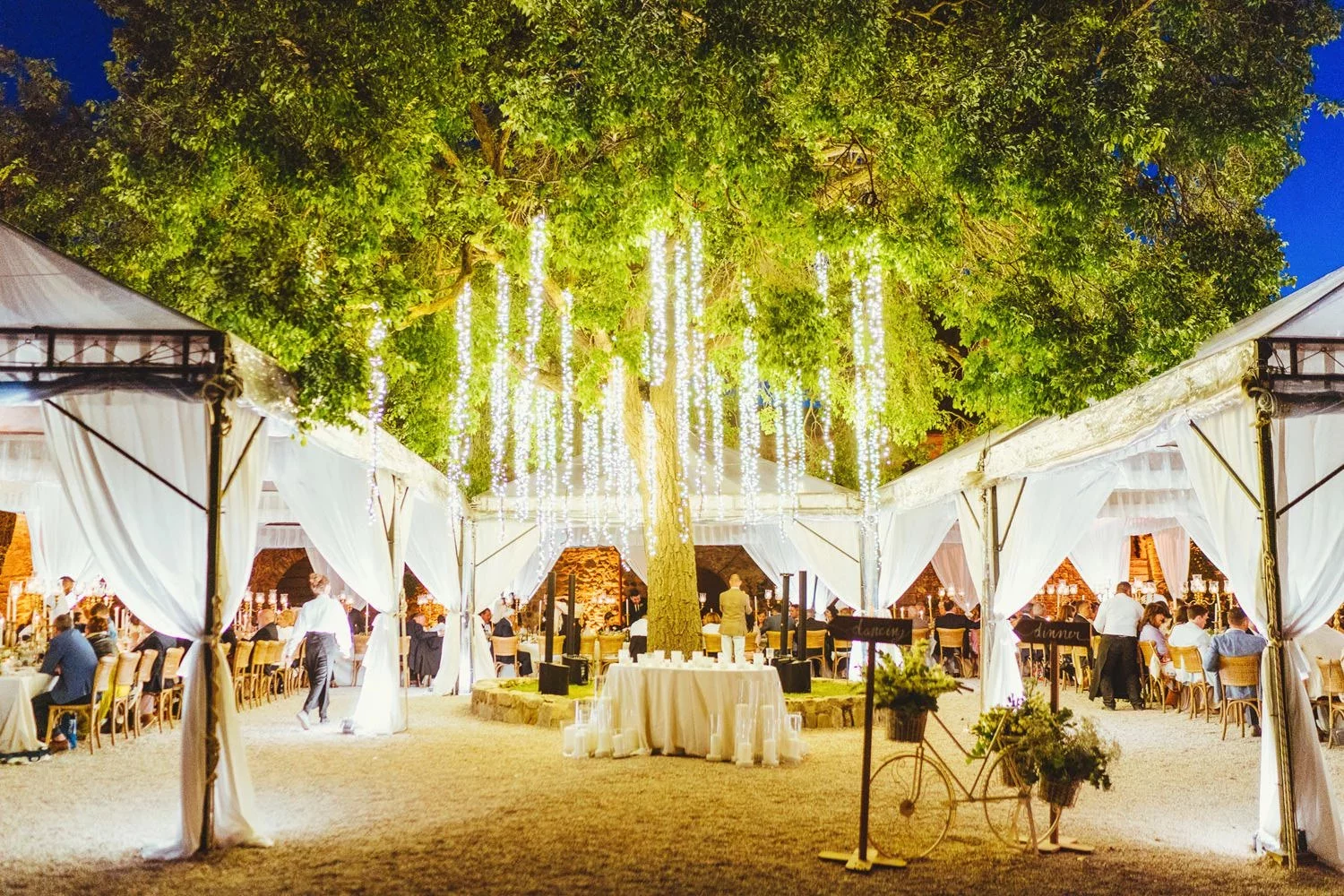 Beautiful lights hang from trees as evening falls upon a wedding celebration at Borgo Di Castelvecchio, one of the most popular wedding venues in Europe.